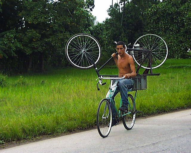 A man on a bike carries another bike in Cuba's western countryside
