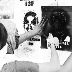 Protester spray-painting a stencil of a dead protester's face on a wall