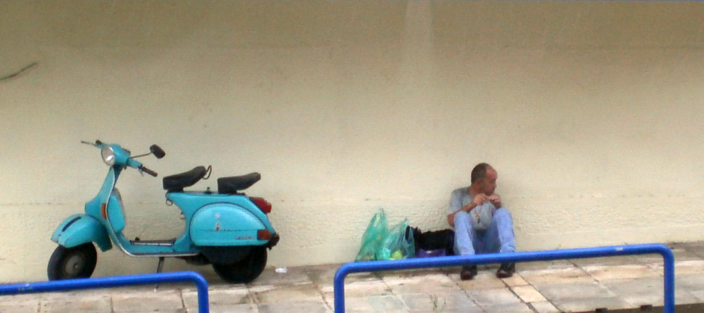 Homeless Polish immigrant sitting on the sidewalk next to a moped