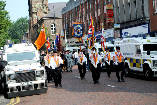 Men carrying Union Jack and other flags, flanked by police vehicles