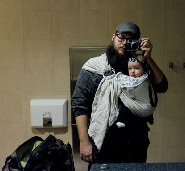 Father with baby in sling snapping photo in the mirror of a bathroom/changing room
