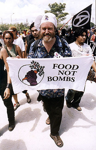 Man in chef's hat carrying Food Not Bombs cloth sign