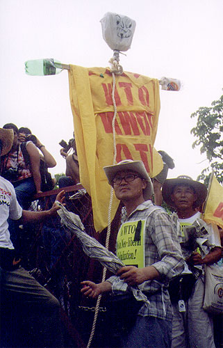 Korean farmers wearing hats and carrying an effigy with the words "WTO"