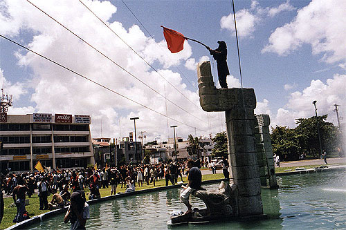 Protester stands on a fountain monument and waves a red flag