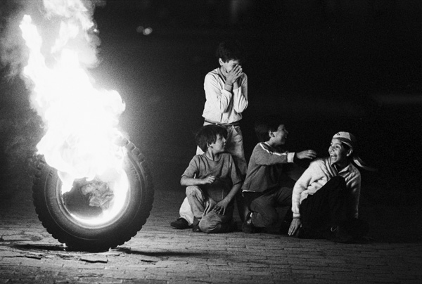 Four children laugh as a tire burns